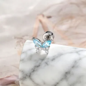 Macro detail of a titanium butterfly stud earring with blue gemstones on marble