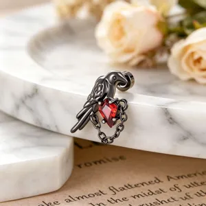 Close-up of bird earring with red diamond-shaped zircon on marble surface
