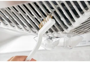 Détail d'une brosse à poils durs nettoyant un filtre de hotte de cuisine avec de la mousse
