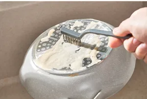 Détail de la brosse métallique nettoyant les taches tenaces sur le fond d'une casserole.