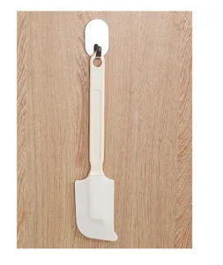 Vollansicht eines cremefarbenen Silikon-Backspatels, der an einem Holzhaken hängt