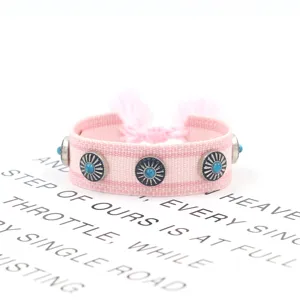Detailaufnahme von rosa handgewebtem Armband mit Metallnieten und blauen Steinen