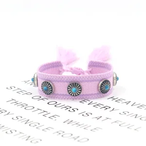 Detailansicht eines lila gewebten Armbands mit Metallnieten und Türkissteinen