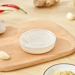 Detalle de un miniprensador de ajos manual blanco sobre una tabla de madera