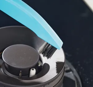 Détail d'une brosse de cuisine bleue nettoyant les fentes d'un brûleur de cuisinière