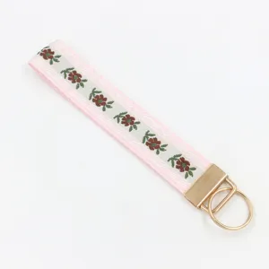 Detailansicht des rosa geblümten Jacquard-Webbandes mit poliertem goldenem Metallschlüsselring.