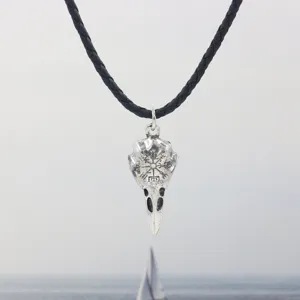 Detailed macro view of a vintage silver Viking raven skull pendant with Norse runes on cord.