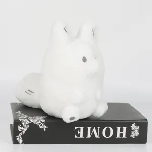 Vue détaillée d'une peluche blanche Anxiety Fox posée sur un livre noir décoratif