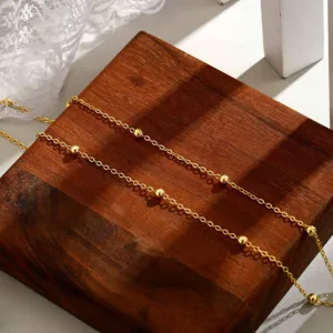 Detaillierte Nahaufnahme einer goldenen Satelliten-Fußkette mit Perlen auf dunklem Holz