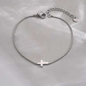 Nahaufnahme eines minimalistischen Silberarmbands mit Boxkette und einem horizontalen Kreuzanhänger