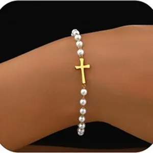 Nahaufnahme eines weißen Perlenarmbands mit goldenem Kreuzanhänger am Handgelenk