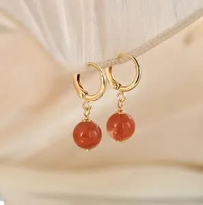 Nahaufnahme eleganter goldener Creolen mit polierten Anhängern aus rotem Achat in weicher Optik