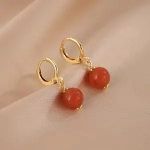 Nahaufnahme goldener Creolen mit eleganten roten Achat-Perlenanhängern auf Seide.