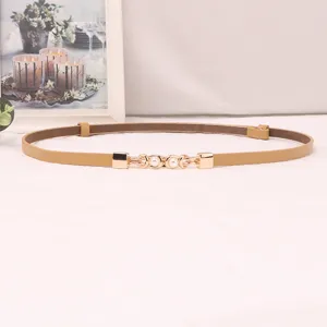 Detail view of thin leather women belt with elegant gold pearl metal buckle on white surface.