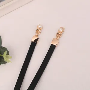Close-up detail of women thin black leather belt with gold metal clasp and pearl decor.