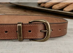 Vintage brown leather belt detailed close-up showing metal buckle and cowhide leather texture.