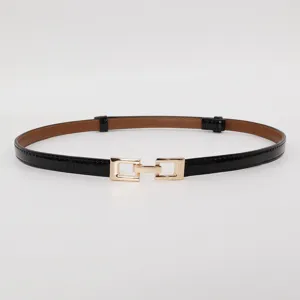 Detailed view of women's thin black patent leather belt with stylish gold square metal buckle.