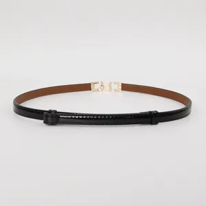 Detail view of women's thin black patent leather belt with elegant gold buckle design.