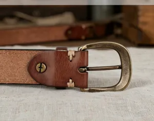 Close-up of brown leather belt with vintage bronze buckle and detailed stitching.