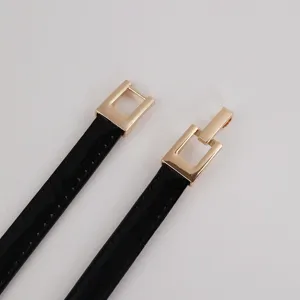 Close-up of women's black patent leather thin belt with gold-tone metal hook buckle detail.
