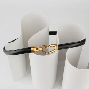 Close-up details of the stylish thin black leather belt featuring gold heart buckle.