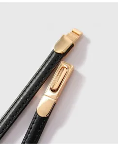Nahaufnahme Detail des dünnen schwarzen Damen Ledergürtels mit eleganter goldener Metallschnalle.