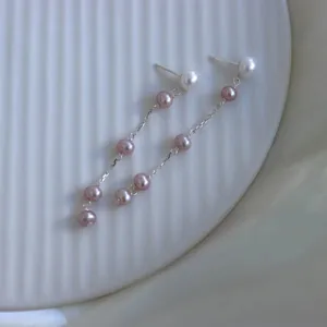 Nahaufnahme eleganter langer Quastenohrringe mit rosa und weißen Perlen an Silberketten
