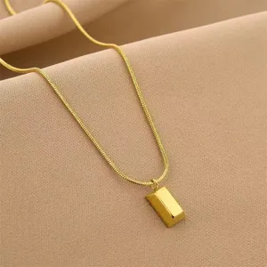 Detailed macro shot of a minimalist titanium steel gold bar pendant necklace on tan fabric
