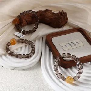 Close-up detail of three elegant smoky quartz bracelets with a citrine bead on a wooden tray.