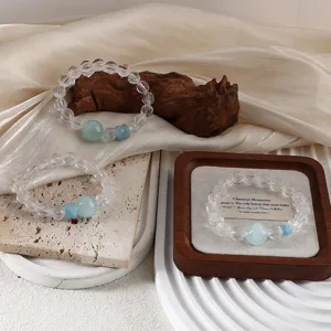 Natural aquamarine and clear quartz beaded bracelets displayed on elegant wooden and stone props.