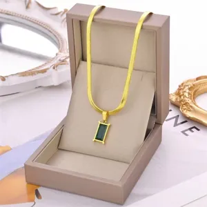 Detailed shot of a gold-plated snake chain necklace with an emerald cut green pendant.