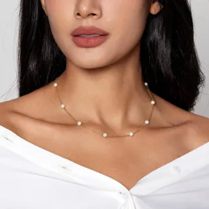 Nahaufnahme einer eleganten Goldkette mit weißen Perlen, getragen von einem Modell.