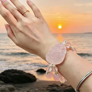 Detailansicht eines rosa Rosenquarz Fuchs-Anhänger-Armbands am Strand bei Sonnenuntergang