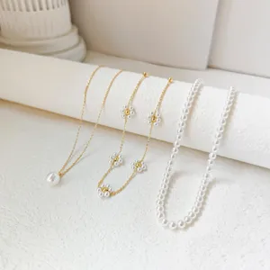 Set aus drei eleganten weißen Kunstperlenketten mit Goldketten und Blumenakzenten.