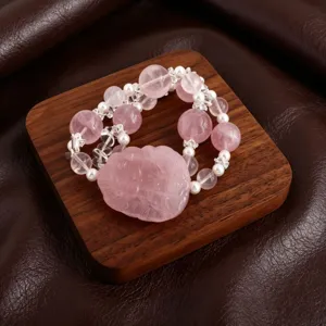 Detailansicht eines rosa Rosenquarz-Perlenarmbands mit geschnitztem Fuchshänger auf Holz.