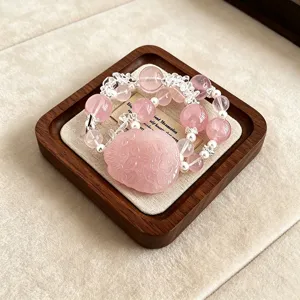 Makroansicht eines rosa Kristallarmbands mit Blumenschnitzerei auf einem Holztablett