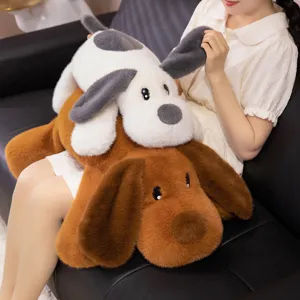 Peluche de chien à longues oreilles douce tenue par un mannequin sur un canapé, tailles variées.