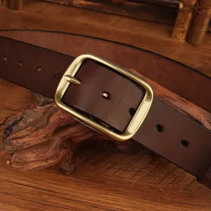 Close up of vintage brown leather belt with brass buckle on rustic wooden background.