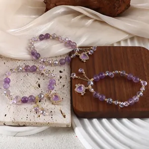Nahaufnahme von drei lila Amethyst-Perlenarmbändern mit Herzanhängern auf natürlichen Requisiten.