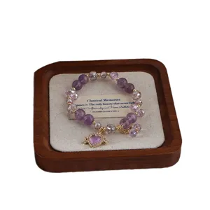 Amethyst Perlenarmband mit goldenem Herzanhänger auf einem rustikalen Holzschmucktablett