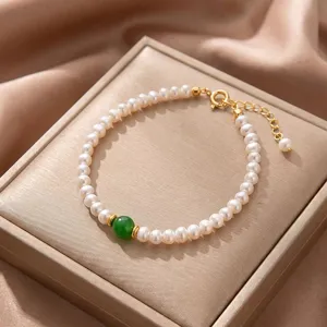 Elegant close-up of a natural white pearl bracelet with a green gemstone on a satin display box