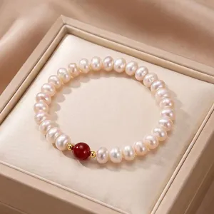 Close-up of a natural pearl bracelet with a central red bead on a jewelry cushion