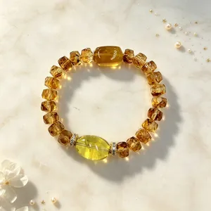 Nahaufnahme eines facettierten gelben Bernstein-Kristallarmbands mit grünem Edelstein.