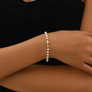 Elegantes weißes Perlenarmband mit einem minimalistischen goldenen Kreuzanhänger am Handgelenk.
