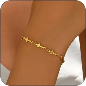 Nahaufnahme eines minimalistisch vergoldeten Armbands mit kleinen Kreuzanhängern am Handgelenk.