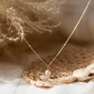 Detailansicht einer eleganten goldfarbenen Kette mit Perlenanhänger in Tropfenform.