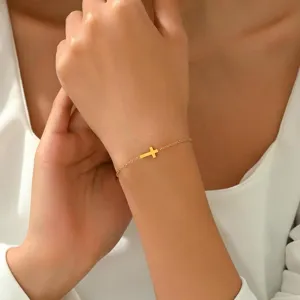 Detaillierte Makroaufnahme eines zierlichen goldenen Kreuzarmbands am weiblichen Handgelenk