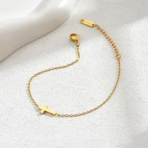 Detailansicht eines minimalistischen vergoldeten Kreuzanhängers an einem feinen Gliederkettenarmband.