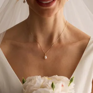 Nahaufnahme einer eleganten goldenen Halskette mit Perlenanhänger bei einer Braut im Kleid