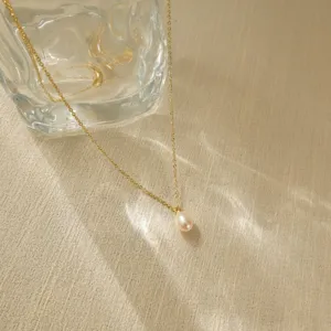 Detailansicht einer goldenen Halskette mit einem eleganten weißen Perlenanhänger.